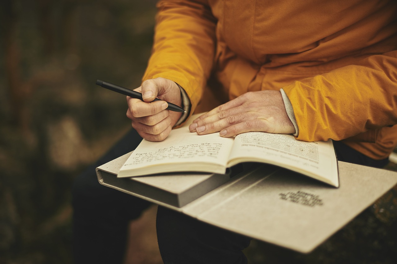 a person in a yellow top writing in a notebook or journal.