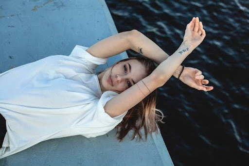 A girl laid on her back on a pier, her arms crossed above her head and the sea in the background