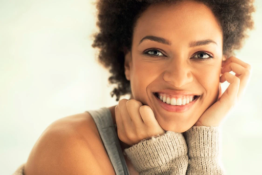 A pretty lady smiling at the camera. She has brown curly hair and looks to be in her 20s